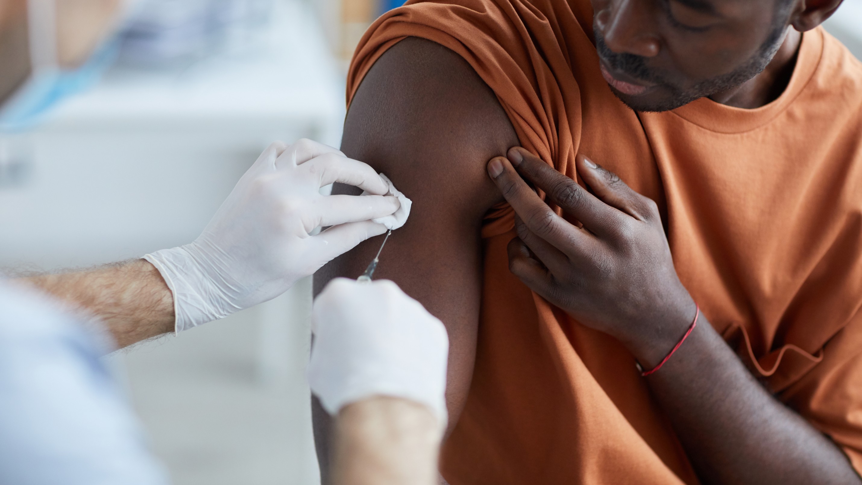 Close up of unrecognizable male nurse injecting vaccine in shoulder of African-American man during covid vaccination in clinic or hospital, copy space