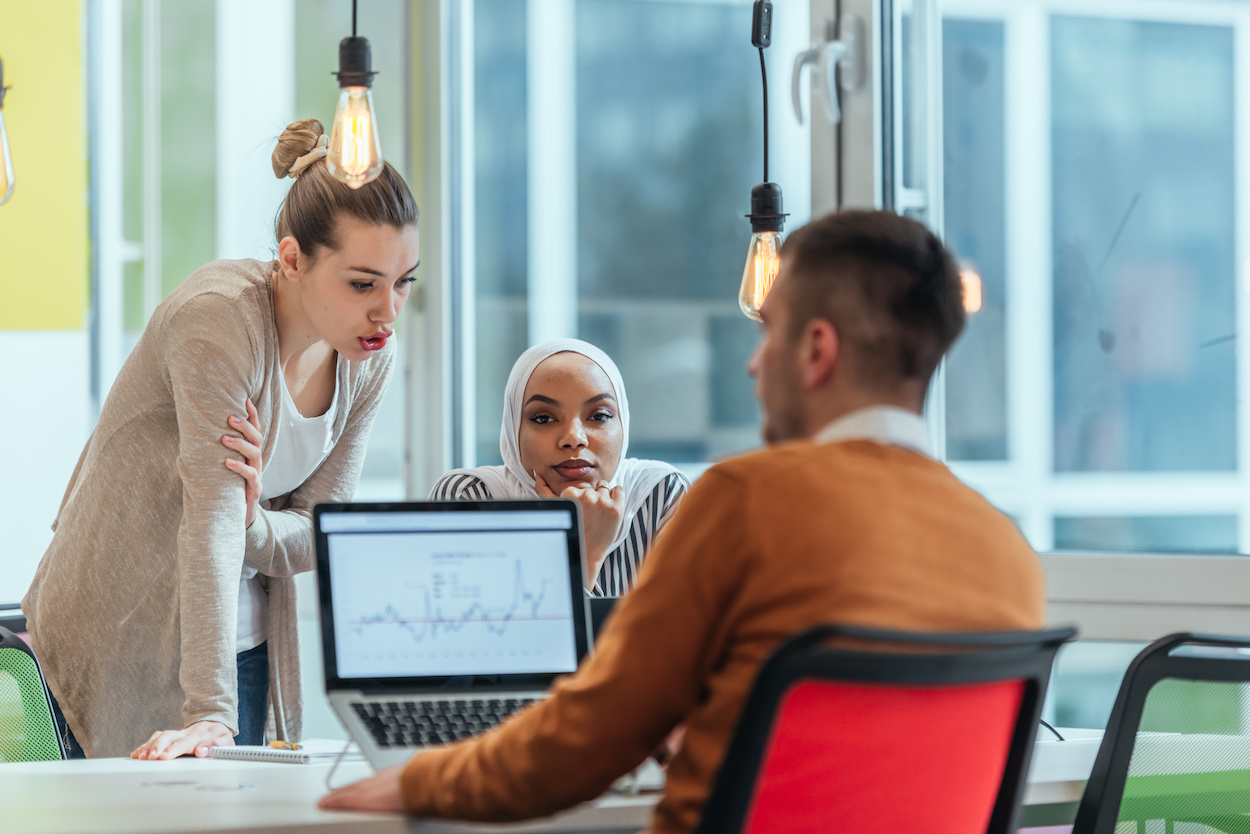 Group of coworkers, teammates helping their new African American, black, muslim colleague wearing hijab to integrate into the modern company. Multiethnic colleagues in a modern startup company.