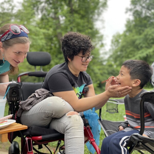 Smiling people paint a child's face