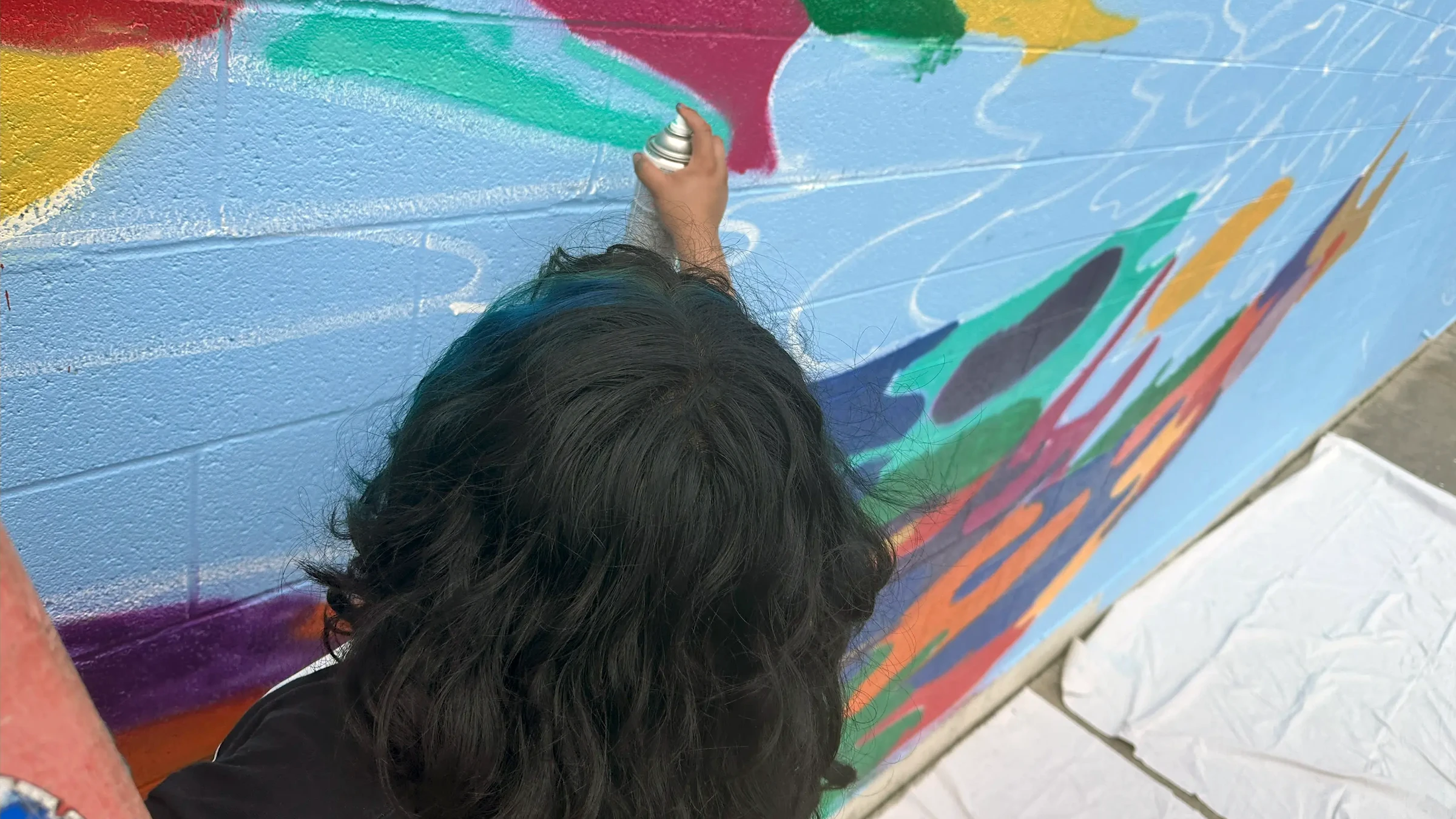 Muralist spray paints on a wall