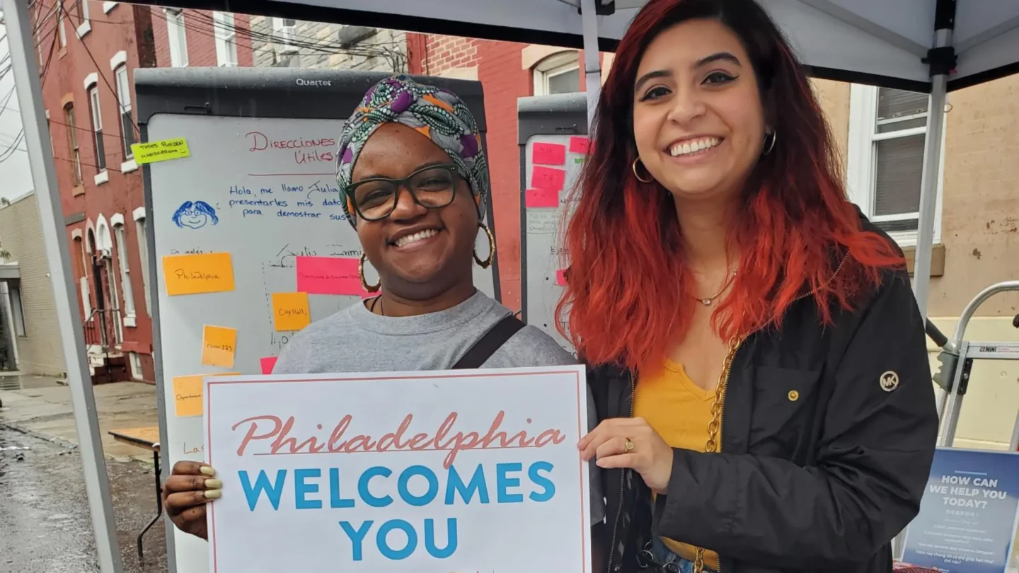 Two women smile and hold a sign that says "Philadelphia Welcomes You"