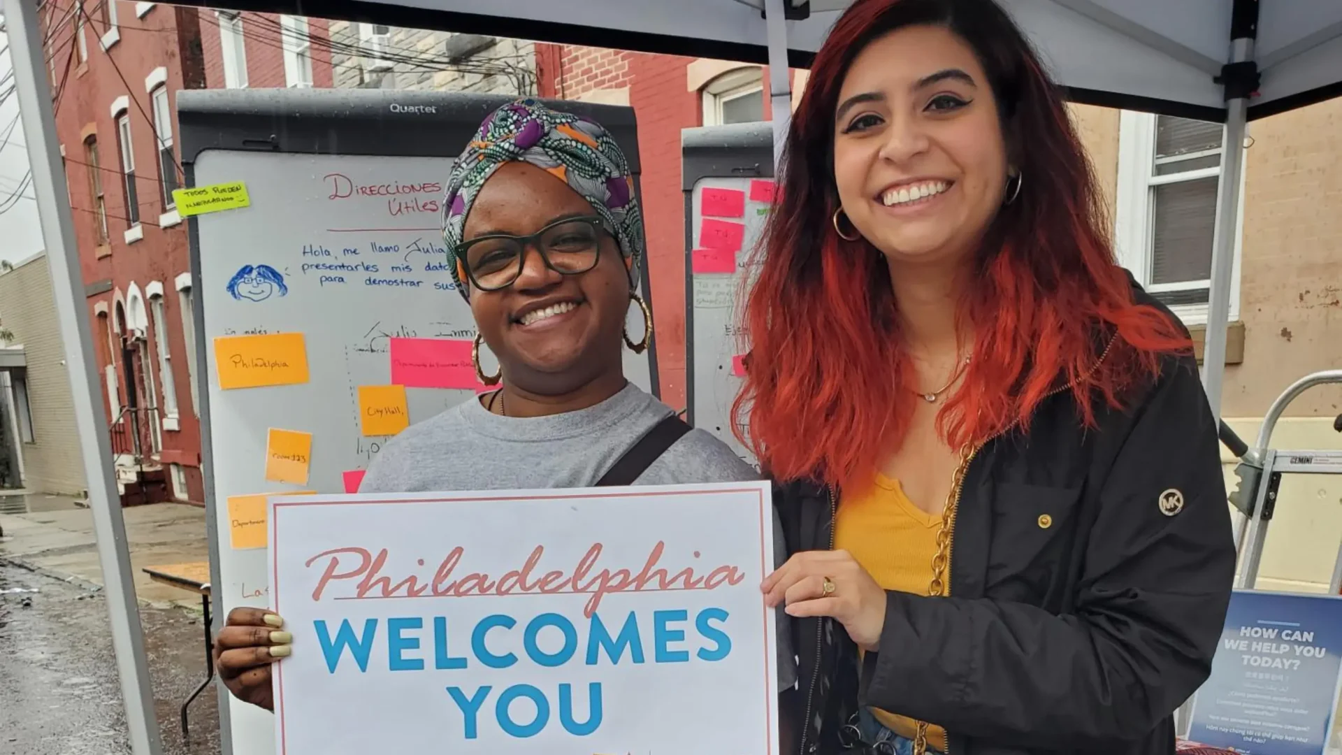 Two women smile and hold a sign that says "Philadelphia Welcomes You"