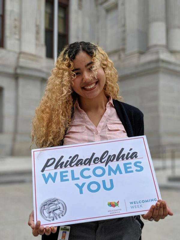 Woman smiles and holds a sign that says "Philadelphia Welcomes You"